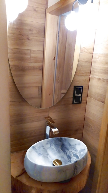 Lustro, umywalka marmurowa, bateria umywalkowa i korek w kolorze złotym, drewniany blat.