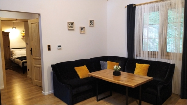 Bieszczady - Domek nad stawem - Czarna sofa i drewniany stół w części salonowej.