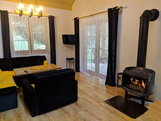 Salon z kominkiem, czarna sofa i fotel, drzwi tarasowe.