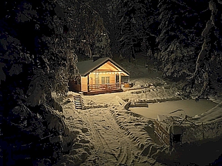 Bieszczady - Domek nad stawem - nocne zdjęcie domku z promieniami światła wylatującego przez okna.